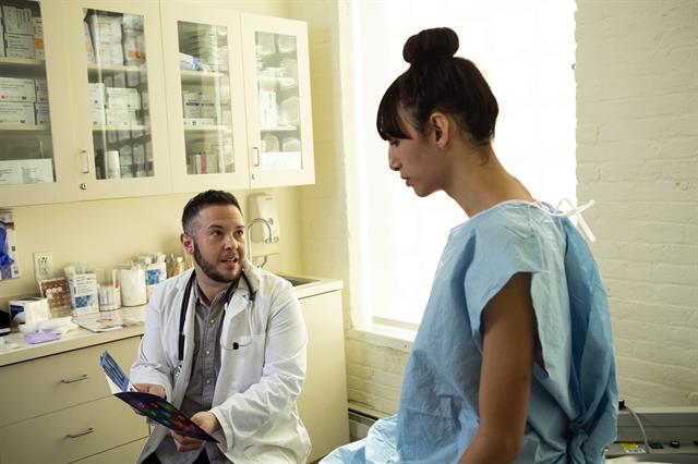 A Transgender Woman in a Hospital Gown Speaking to her Doctor a Transgender man in an exam room
