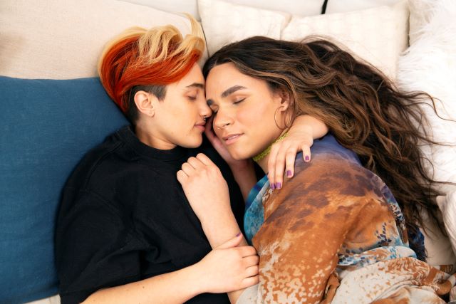 A transmasculine gender nonconforming person and transfeminine nonbinary person sleeping together in bed